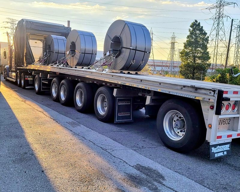 Three steel coils chained on a Fission trailer, cover rolled back for loading