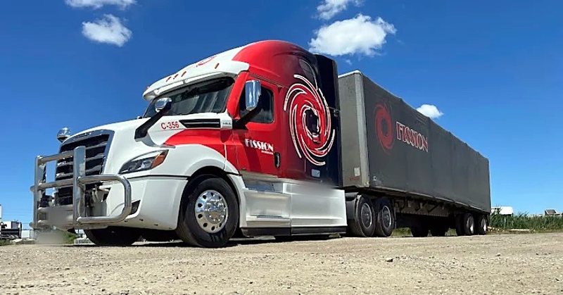 Fission tractor pulling a tarped trailer with the Fission logo on the tarp