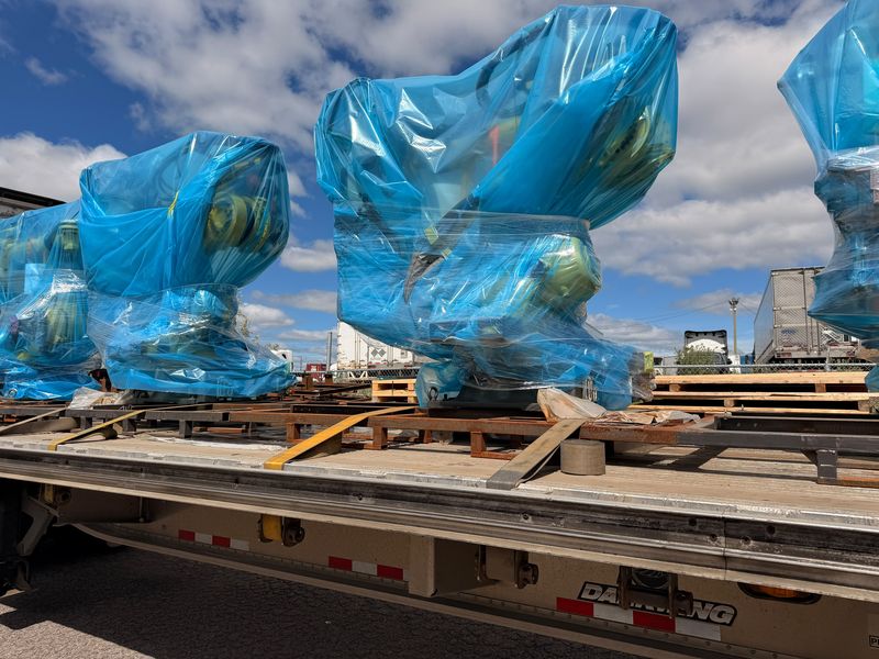 Industrial robots wrapped in blue plastic, strapped on skids on a Fission flatbed